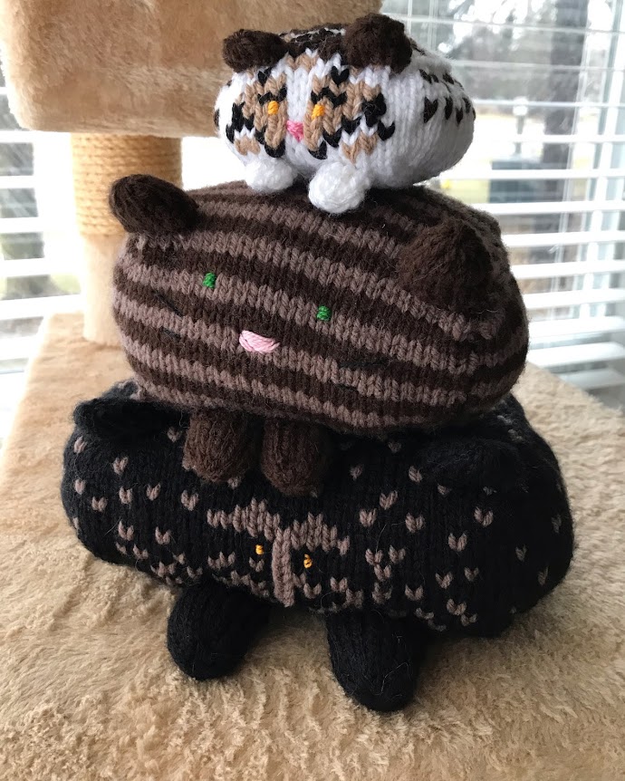 Three knit cats stacked on top of each other. All a different size and pattern.